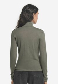 Olivgrön polotröja med långa ärmar, slim fit, ribbade manschetter och nederkant, lättstickad textur. Modellen visas bakifrån.