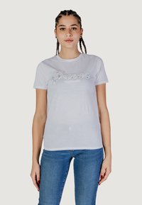 T-shirt bianco a maniche corte con un logo testurizzato in strass argento, abbinato a jeans blu. Stile leggero e aderente.