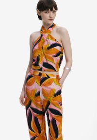 Top con collo all'halter e pantaloni abbinati in un vivace rosa con una grande stampa floreale arancione. Tessuto leggero con una texture liscia e tasche visibili.