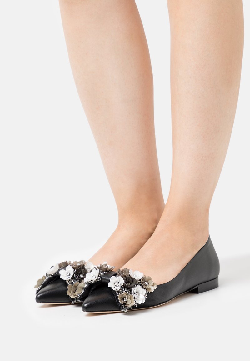 Ballerines noires à bout pointu portées aux pieds, décorées d'ornements floraux noirs, blancs et gris à l’avant.