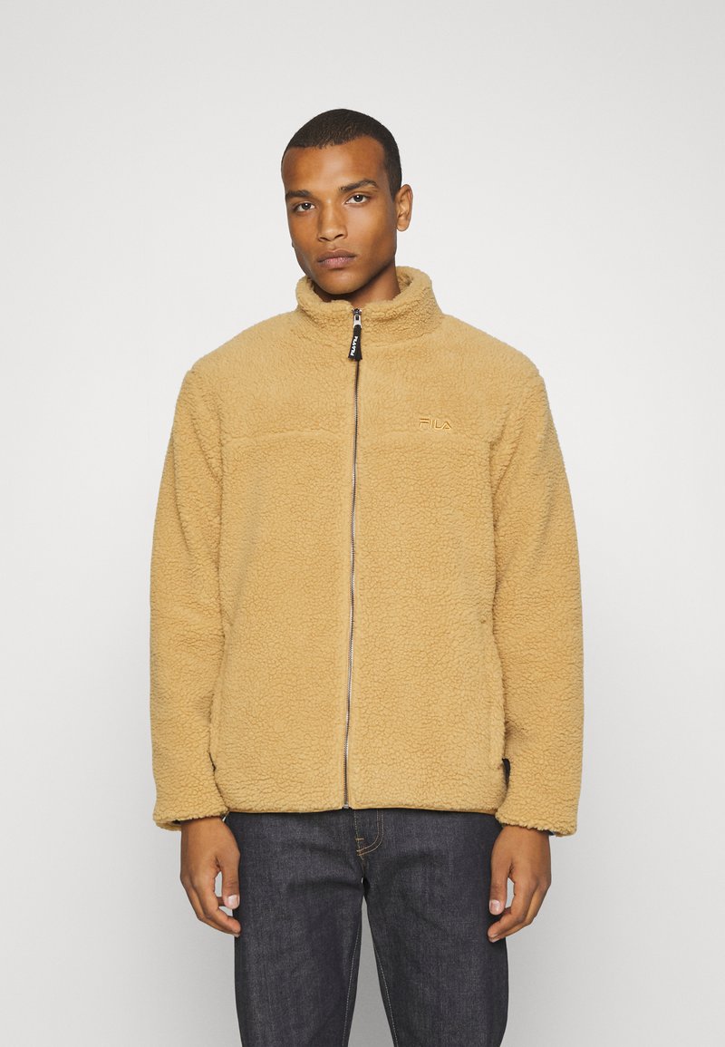 Giacca in pile beige con colletto alto, zip a tutta lunghezza e logo FLIA sul petto. Presenta un tessuto testurizzato e polsini elasticizzati.