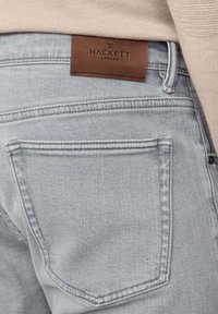 Svijetloplave traperice s kožnom oznakom "HACKETT LONDON" na pojasu, sa standardnim stražnjim džepovima i detaljima u šivanju.