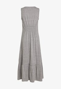 Sukienka bez rękawów w odcieniu szarym ma dopasowaną górę z marszczeniem, rozkloszowaną spódnicę z falbaną oraz jest wykonana z miękkiego, elastycznego materiału.