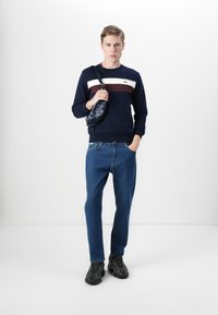 Marine genser med hvite og burgunder horisontale striper, kombinert med blå denimjeans. Svart crossover-veske og mørke mønstrede sko.