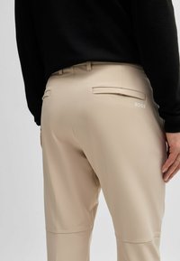 Pantaloni beige realizzati in tessuto liscio, dotati di due tasche posteriori e un piccolo logo "BOSS" bianco sul lato destro.