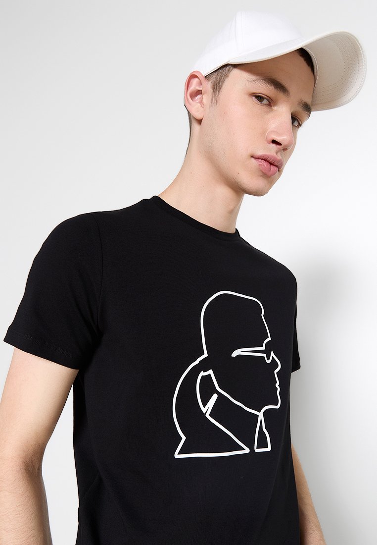 Camiseta negra de algodón, con un diseño gráfico de perfil en contorno blanco y gafas. Modelo que lleva una gorra blanca.