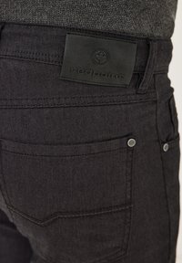 Black jeans with a textured pattern, featuring a leather tag embossed with "redpoint" and visible metal buttons on the pockets.