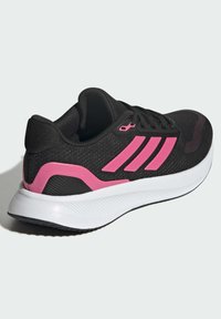Black athletic shoe with pink accents, textured fabric upper, three-stripe design, and a white midsole with ribbed detailing.