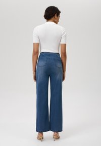 Hooggewaisted blauwe denim wijde pijpen jeans met twee achterzakken en een subtiele vervaging. Gepaard met een fitted witte geribbelde top.