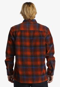 Rød og sort rutet flannel skjorte med blå accenter, med lange ærmer, knapmanchetter og spids krave. Bagfra vises.