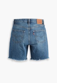 Shorts en denim bleu coupés avec ourlets effilochés, deux poches arrière, détails de couture et une étiquette de marque en cuir sur la ceinture.