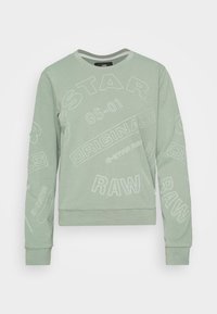 Sudadera verde menta con cuello redondo y mangas largas. Presenta texto y logotipos bordados en blanco. Tejido suave y texturizado con un corte holgado.