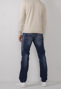 Maglione a maglia color beige chiaro, jeans in denim blu con sfumature, due tasche posteriori e sneakers bianche. Vestibilità standard e design a gamba dritta.