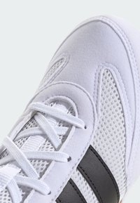 Bílé sportovní boty s prodyšnými panely, měkkými semišovými akcenty a černými pruhy podél strany. Zavazovací na ploché bílé tkaničky.