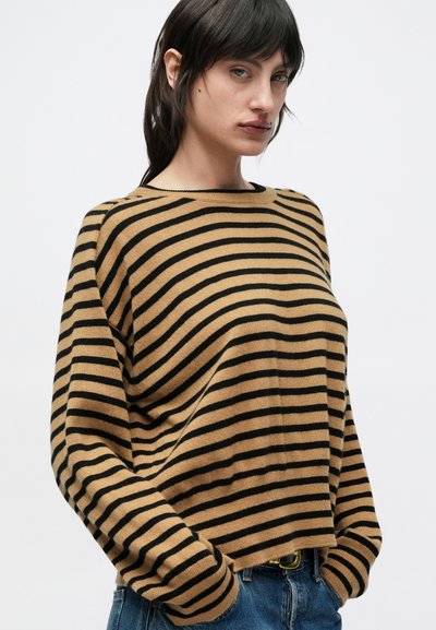 Καφέ και μαύρο ριγέ πουλόβερ με μακριά μανίκια, άνετη εφαρμογή και ριμπ λαιμόκοψη, συνδυασμένο με μπλε τζιν παντελόνι.