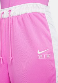 Rozā šorti, kas izgatavoti no viegla auduma, ar baltām sānu panelēm, stringa jostasvietu un izšūtu Nike logo ar vārdu "AIR."