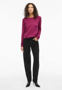 Maglione fucsia con polsini a coste, abbinato a jeans neri a vita alta e décolleté nere a punta. Texture liscia e design semplice.