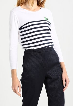 Weißes Langarmshirt mit navyblauen horizontalen Streifen und einem kleinen grünen gestickten Design, kombiniert mit strukturierten navyblauen Hosen.