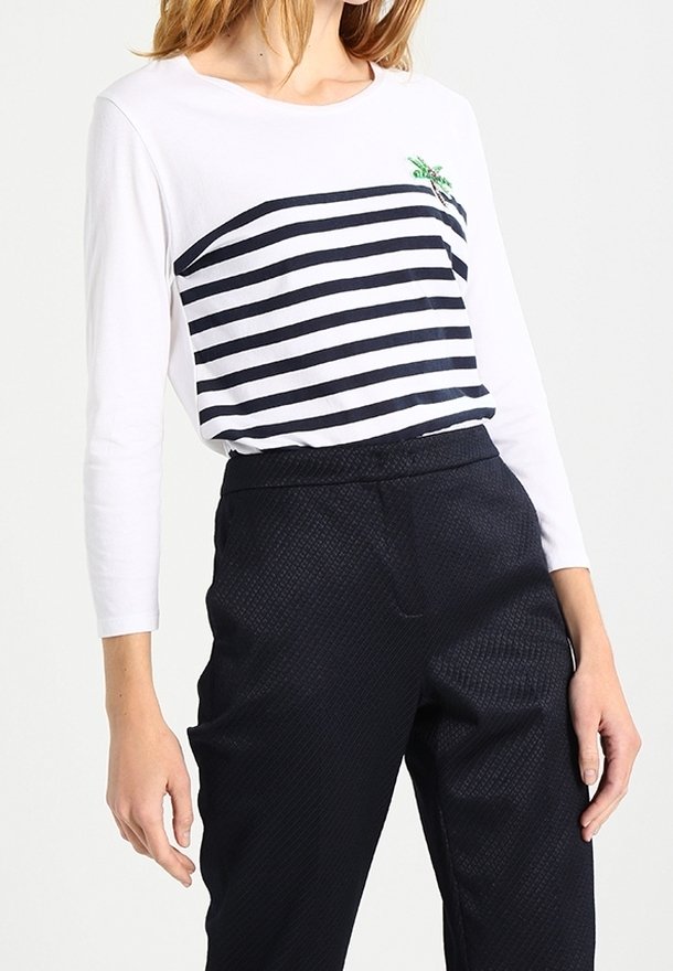 Maglietta bianca a maniche lunghe con righe orizzontali blu marine e un piccolo motivo ricamato verde, abbinata a pantaloni blu navy a trama.
