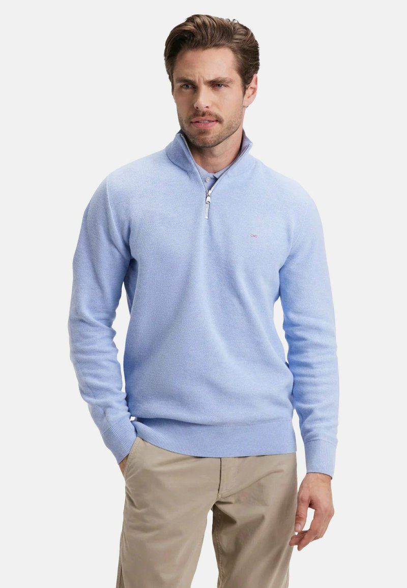 Sweat à zip bleu clair en tricot texturé ; avec un col montant et des poignets et un ourlet côtelés ; associé à un pantalon beige.