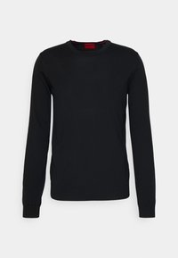 Pull noir à manches longues en tissu tricoté lisse, avec un col rond et des poignets côtelés. Présente une étiquette rouge au niveau du col.