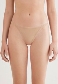 Nude microvezel string met dunne elastische tailleband en benen. Lichtgewicht, naadloos ontwerp biedt minimale bedekking.