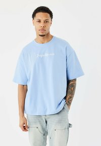 Camiseta de manga corta azul claro con un corte relajado, que presenta diseños de cactus bordados en blanco y el texto "Projectparis" en la parte frontal.