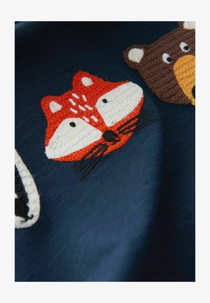 Tekstils, kurā attēlotas dzīvnieku portreti: sarkanais lapsa, brūnais lācis un melnbalts raķets. Izšūts ar krāsainām, teksturētām dzijas uz tumši zilas fona.