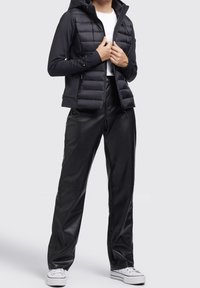 Schwarze gesteppte Jacke mit Kapuze, Reißverschluss und langen Ärmeln, kombiniert mit schwarzen Kunstlederhosen und weißen Turnschuhen.