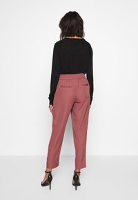 Zwart langemouwen top gecombineerd met roze, tapered broek met een elastische tailleband en twee achterzakken. Stiletto hakken maken de look compleet.
