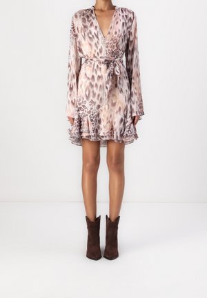 Mujer con un vestido de manga larga estampado de animales, con cinturón de lazo y volante en el dobladillo, combinado con botines marrones, sobre un fondo liso.