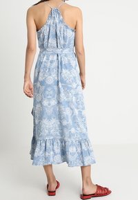 Jasnoniebieska maxi sukienka w kwiaty z falbaną u dołu, regulowanymi ramiączkami i dopasowanym pasem w talii. Ma delikatny biały wzór w całej sukience.