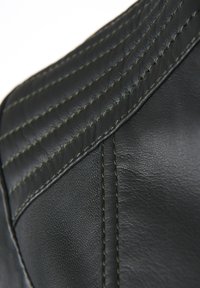 Svart läder med en strukturerad finish, med en kviltad design och kontrasterande gröna sömmar längs sömmarna. Närbild.