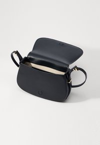 Borsa in pelle blu navy, dalla forma arrotondata, con hardware dorato e una tracolla singola. Il design aperto svela un interno beige. Include una chiusura a bottone.