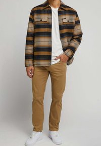 Bruin en marineblauw geruit flanellen overhemd met twee borstzakken, gecombineerd met kaki broek en witte sneakers. Gladde textuur, casual stijl.