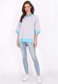 Randig oversized tröja i ljus rosa och blått, med korta ärmar och rundad nederkant. Kombinerad med ljusblå skinny jeans och vita sneakers.