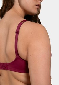 Soutien-gorge bordeaux avec des bretelles ajustables et un système de fermeture à agrafe au dos, fabriqué en tissu lisse et avec un léger éclat.