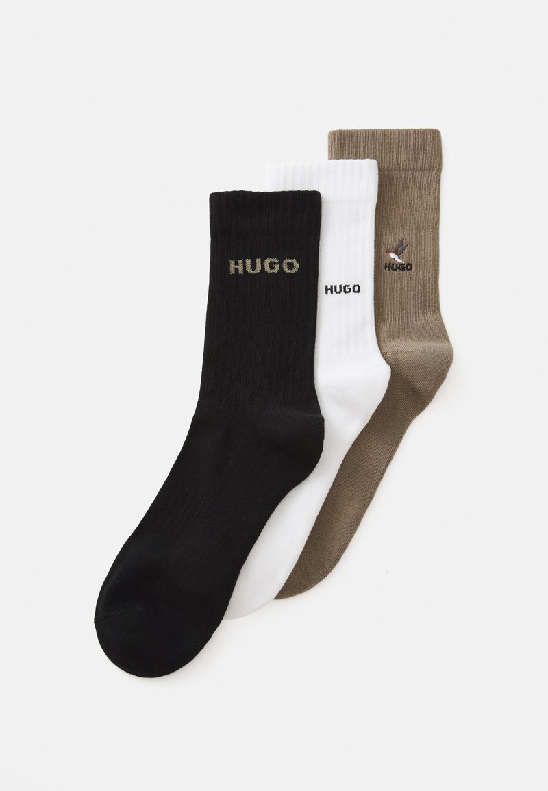 Drei gerippte Socken in Schwarz, Weiß und Braun, jede mit "HUGO"-Branding; die braune Socke hat einen gestickten Vogel über dem Markennamen.