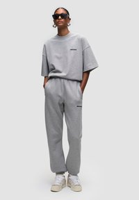 Grijze oversized t-shirt en bijpassende trainingsbroek van zacht katoen, met een logo bij de borst en elastische manchetten op de broek.
