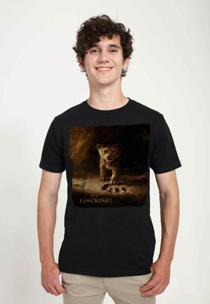 T-shirt nera con una grafica di un cucciolo di leone su uno sfondo sabbioso, con il testo "Il Re Leone" in basso in un font dorato.