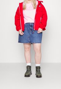 Czerwona lekka kurtka, różowa koszulka z wytłoczonym logo, dżinsowa spódnica i zielone buty na sznurówki z białymi skarpetkami. Prosty design, codzienny styl.