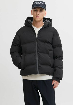 Sort pufferjakke med hætte, med lynlåslukning, brede quiltede sektioner og elastiske manchetter. Laget over en let sweatshirt.
