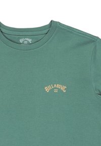T-shirt verde in cotone con scollo rotondo, maniche corte e logo giallo "Billabong" sul davanti. Texture liscia e design semplice.
