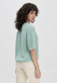 Pull en tricot à manches courtes de couleur vert menthe clair avec un motif texturé et une coupe décontractée. Associé à un pantalon taille haute de couleur crème.
