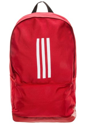 Red fabric backpack with a smooth texture, features three white vertical stripes on the front, a top handle, and a side mesh pocket.