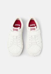 Sneaker bianche in pelle con texture perforata, dotate di lacci elastici e una strap in velcro. Soletta rossa con logo "CAMPER". Punta arrotondata.