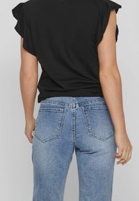 Černý top s krátkým rukávem a volánovými rameny, kombinovaný s světle modrými džíny s vysokým pasem, které mají dvě zadní kapsy a mírně vypalovanou texturu.