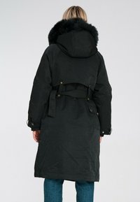 Czarna parka z dużym kapturem z sztucznego futra, paskiem w talii oraz luźnym krojem. Tkanina ma gładką fakturę i matowe wykończenie.