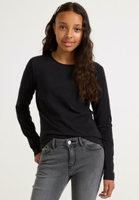 Sort langærmet skjorte i blødt stof, rund halsudskæring, parret med grå jeans med klassisk fem-lommer-design og frontknaplukning.