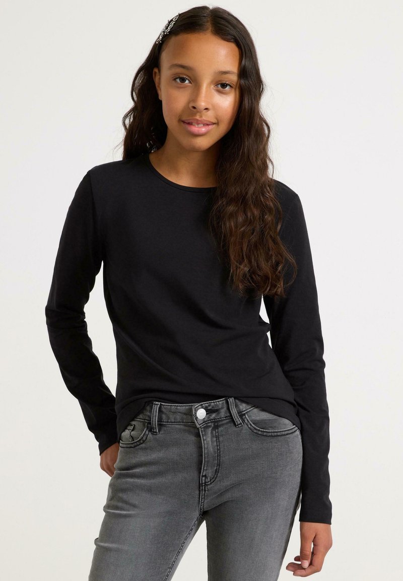 Sort langærmet skjorte i blødt stof, rund halsudskæring, parret med grå jeans med klassisk fem-lommer-design og frontknaplukning.